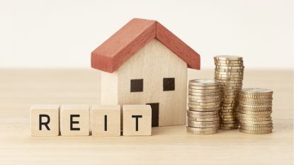 The word REIT sits next to a wooden house and stacks of coins.