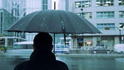 A man holds an umbrella while standing in the rain in front of a downtown building.