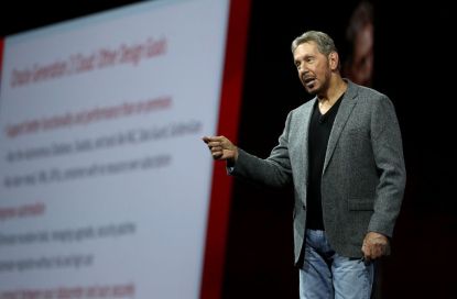 Larry Ellison giving a presentation on stage with screen behind him.